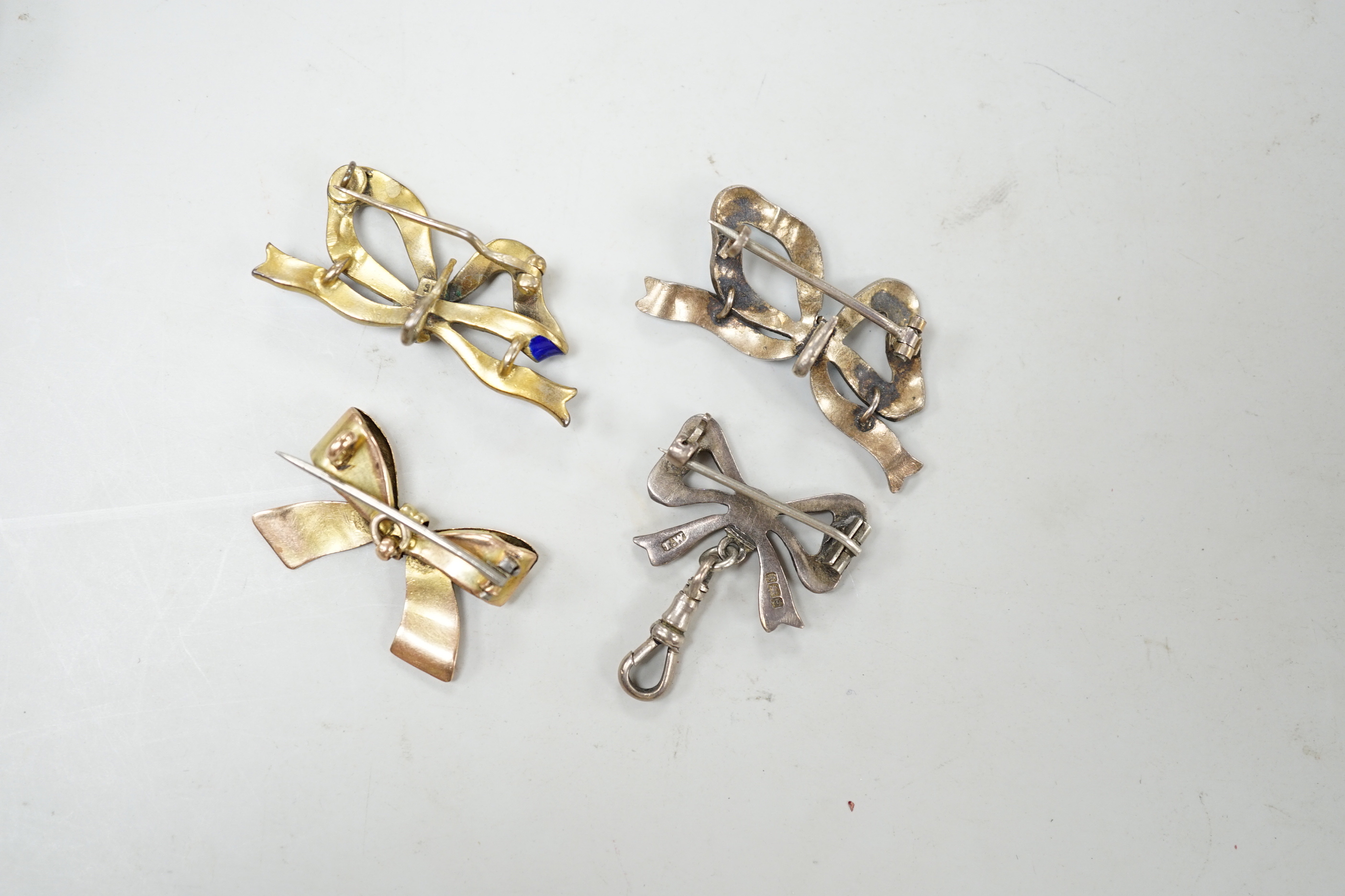 An engraved yellow metal ribbon bow brooch, 26mm, 2.8 grams, together with three silver/gilt white metal and enamel ribbon bow brooches.